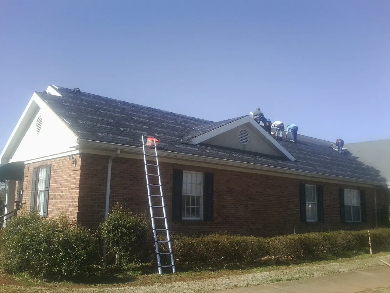 Crew tearing shingles off a brick ranch roof with a ladder set — Emergency Roof Repair work by our crew in Mount Perry