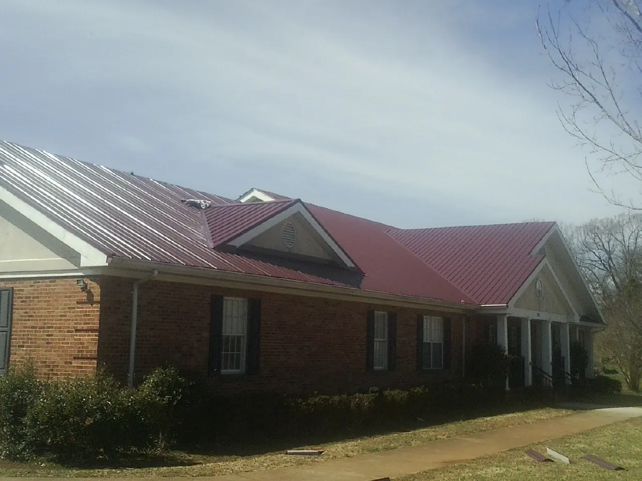 Red metal roof with gabled entries on a long brick building, from a Hail Damage Roof Repair job in Mount Perry