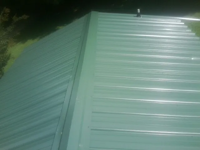 New green metal panels meeting at the ridge of a roof — Flat Roof Repair work by our crew in Mount Perry