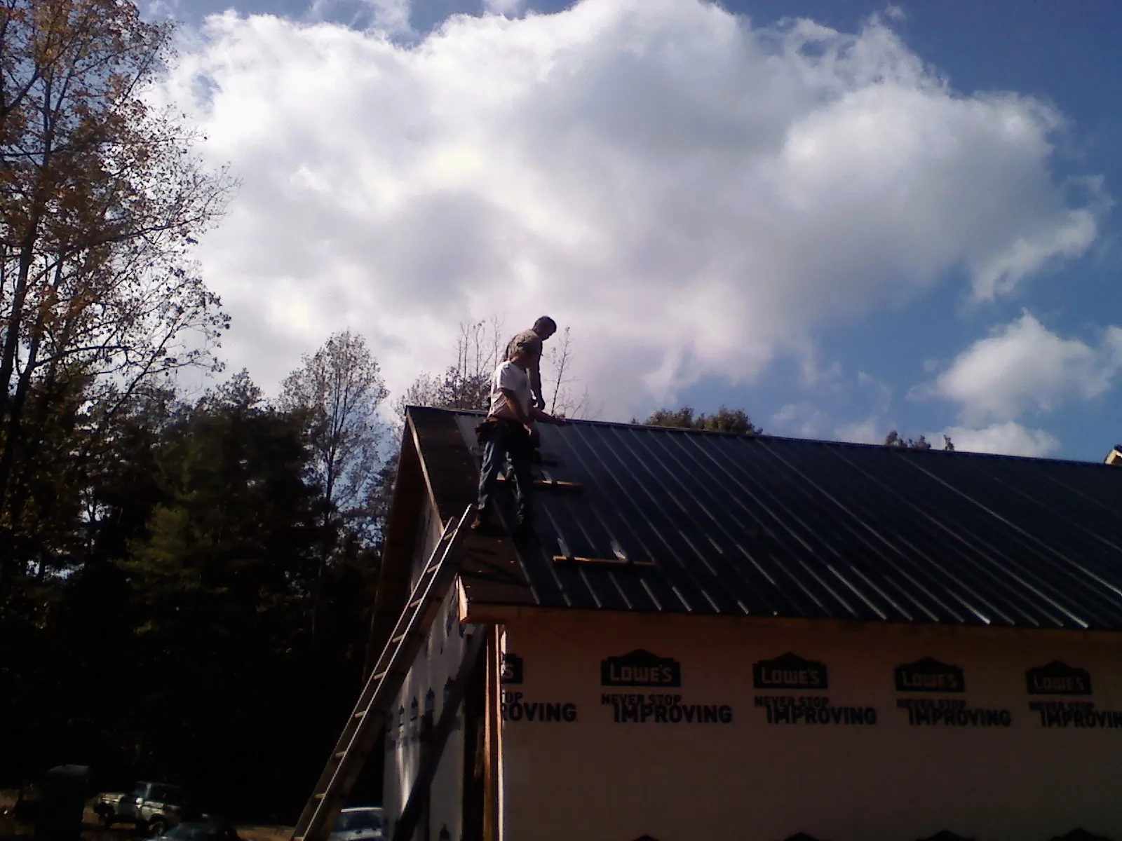 Roofer fastening dark metal panels high against a cloudy sky, from a Roof Inspection job in Mount Perry