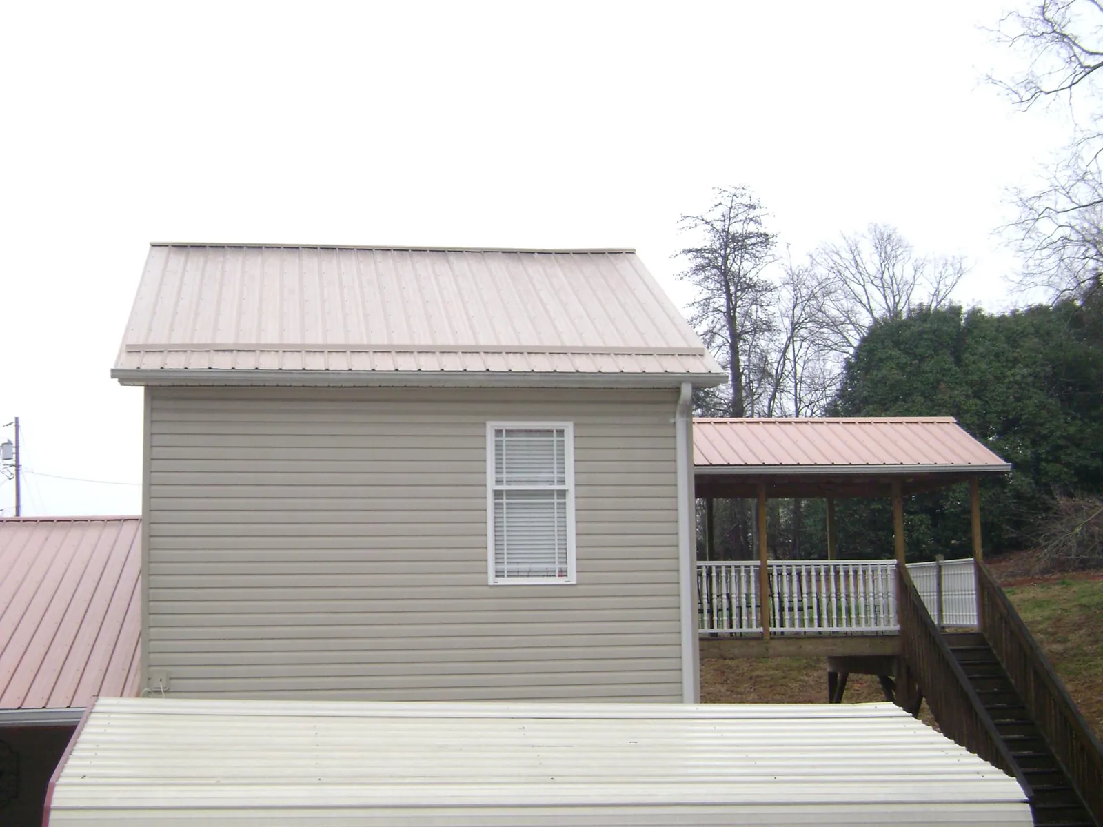 Tan metal roofs on a two story addition and attached porch, from a Roof Replacement job in Mount Perry